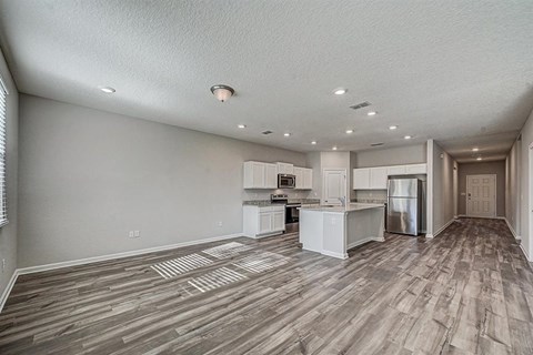 Open-concept living space with gray wood floors, white kitchen cabinets, and stainless steel appliances.