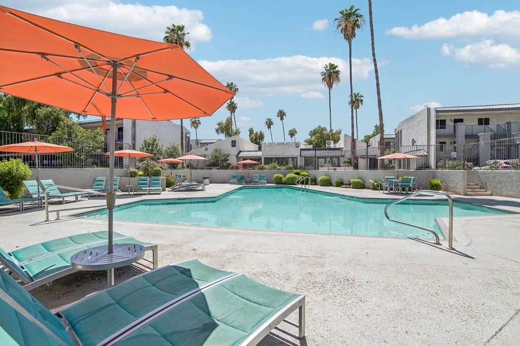 A pool area with a large orange umbrella and lounge chairs.