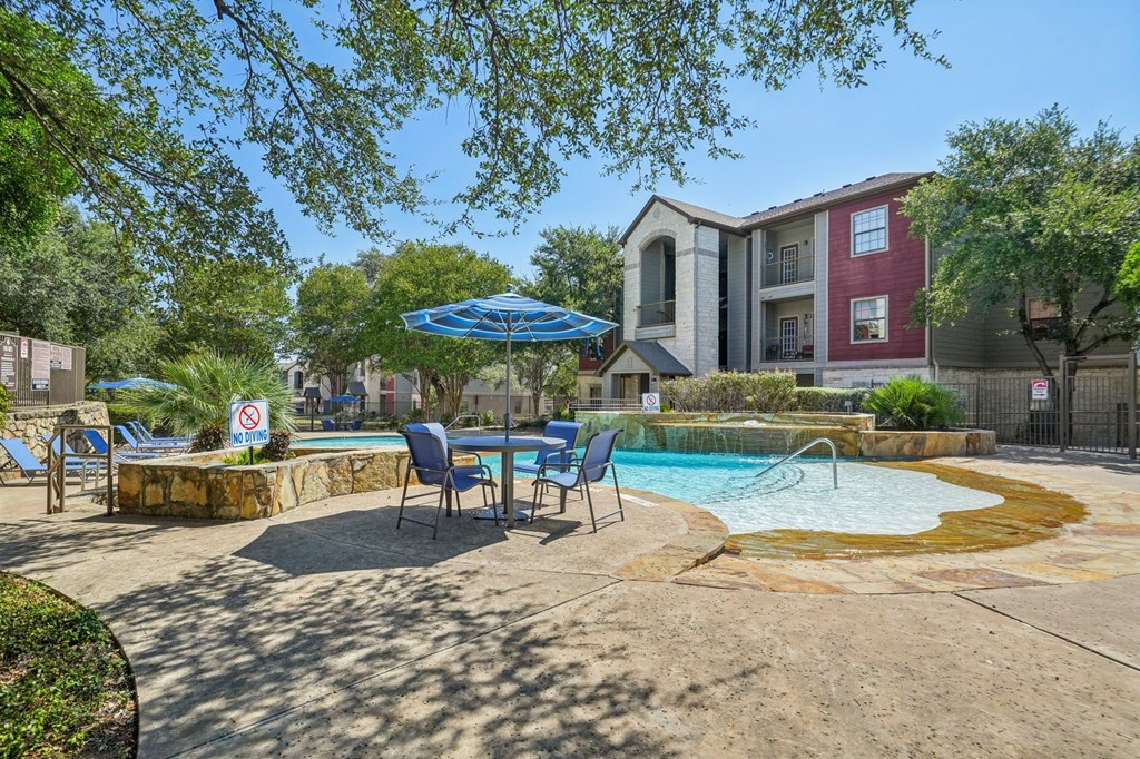A pool area with a blue umbrella and chairs.