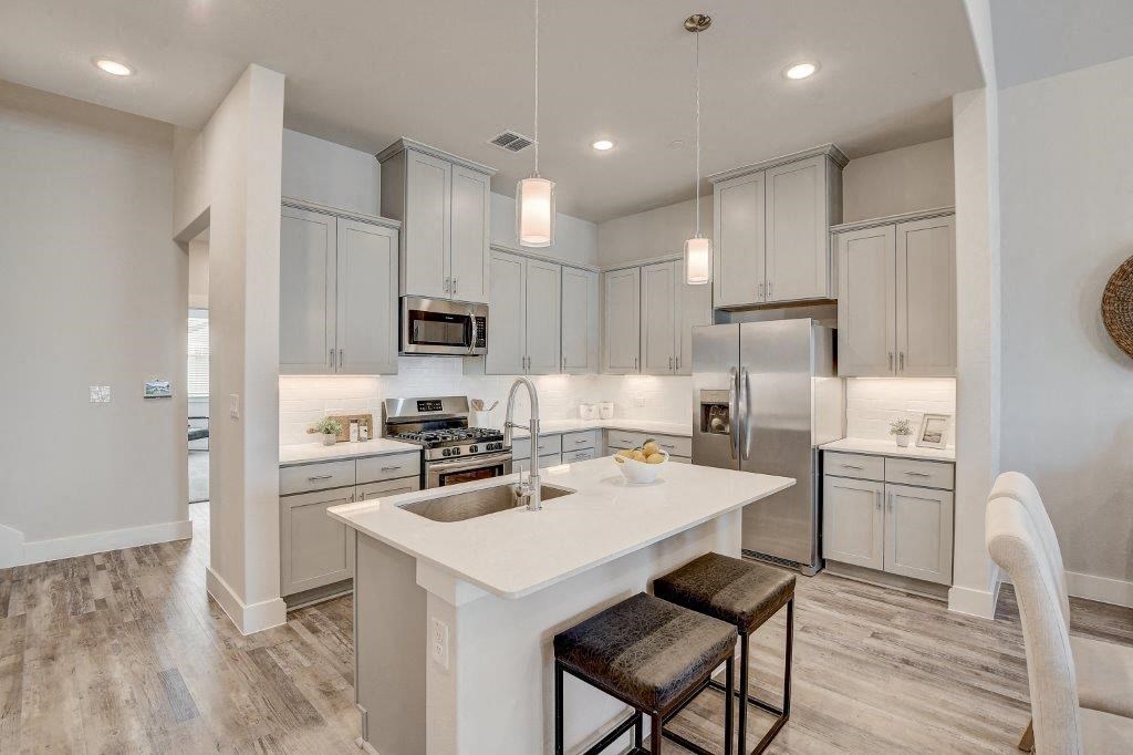 Luxury Single Family Homes in Arlington TX for Rent - Legacy Park at Viridian - Modern Kitchen with White Counters, Large Island with Hanging Lights and Stool Seating, Grey Cabinetry, Stainless Steel Appliances, and Tile Backsplash