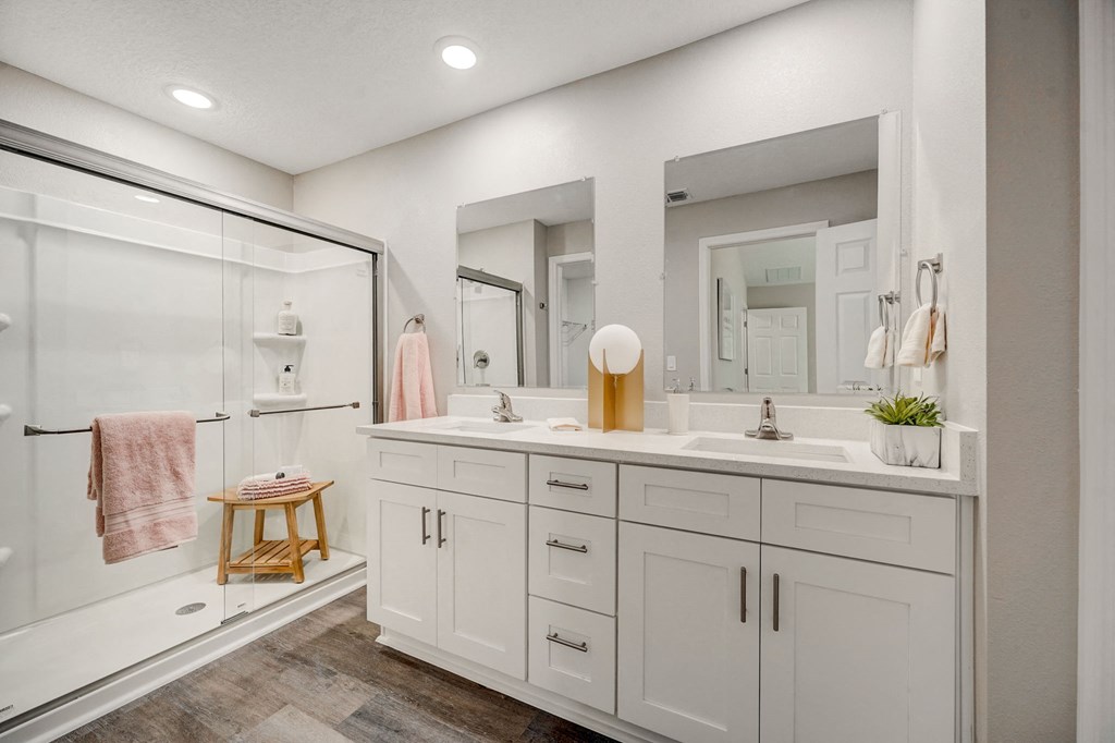White bathroom with two sinks and a shower at The Groves at Lake Ella in Lady Lake, Florida, a pet-friendly rental community.