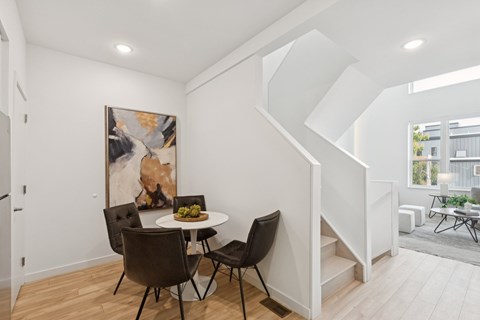 Dining nook with white tulip table, dark tufted leather chairs, gold-framed art, and white staircase ascending to loft