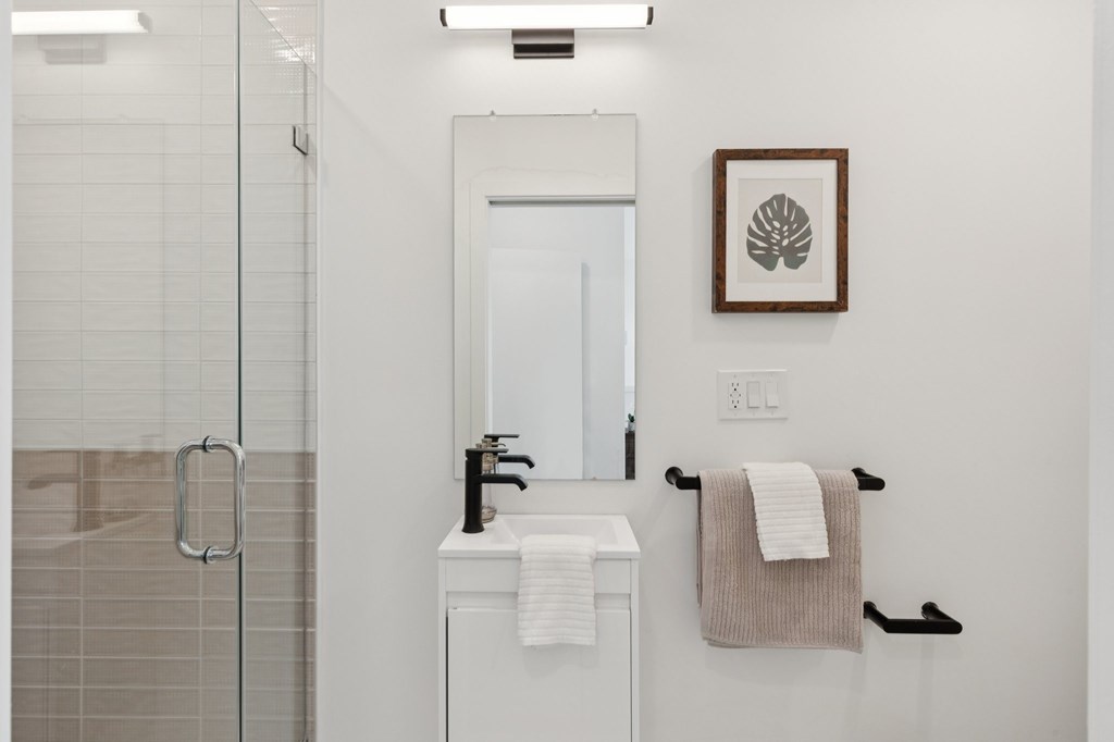 A white bathroom with a glass shower stall and a white sink vanity.