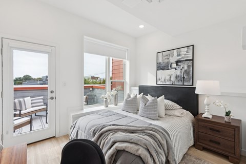 Bedroom with black leather headboard, gray bedding, striped pillows, B&W art, and glass balcony door with rooftop views