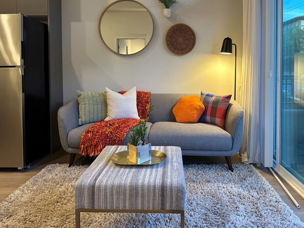 Studio Apartments for Rent Bothell, WA - Morado Bothell - Living Room with Luxury Vinyl Plank Flooring, Area Rug, Grey Couch, Cloth-Covered Coffee Table, Standing Lamp, and Sliding Glass Door with Access to Patio.