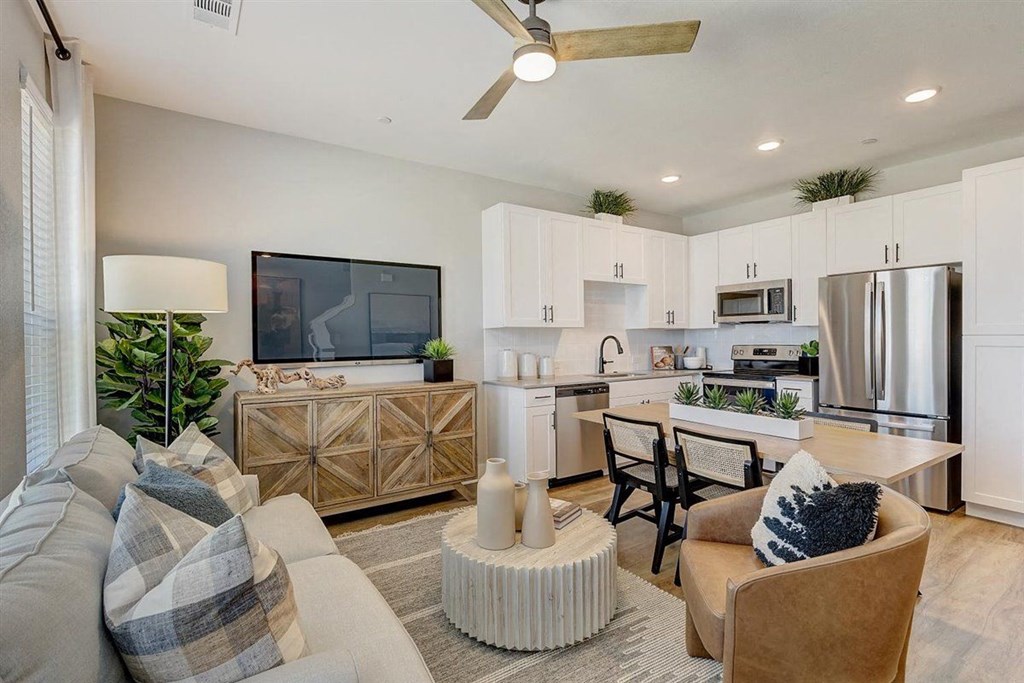 a living room and kitchen with white cabinets and a large tv on the wall