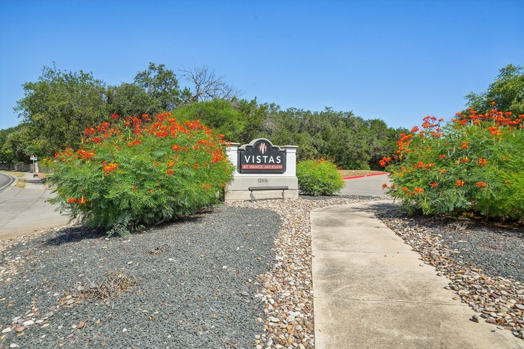 A sign that says "VISITAS" is in front of a bush with red flowers.