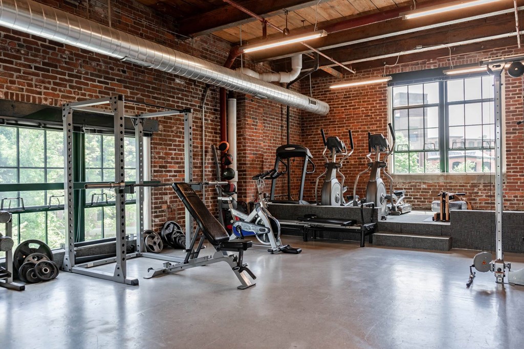 Gym interior with exposed brick, weight rack, and cardio equipment.