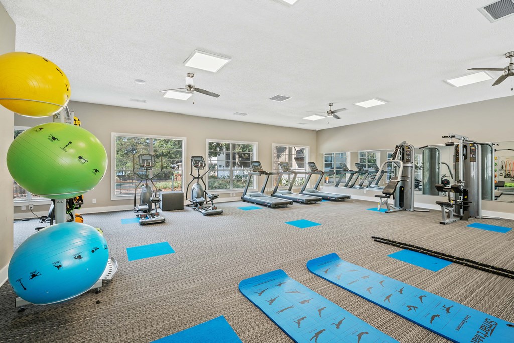 a gym with cardio equipment and exercise balls on the floor