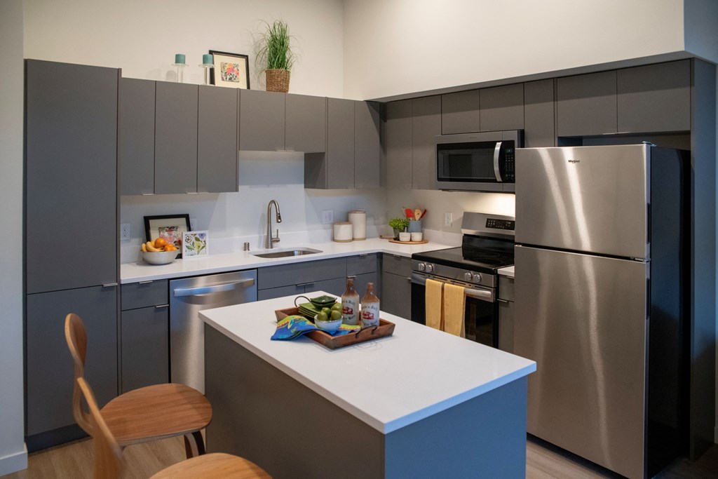 Two-Bedroom Apartments in Bothell, WA - Morado Bothell - Kitchen with Luxury Vinyl Plank Flooring, Stainless Steel Appliances, Grey Designer Kitchen Cabinets, White Quartz Countertops, and Mobile Kitchen Island with Chairs.
