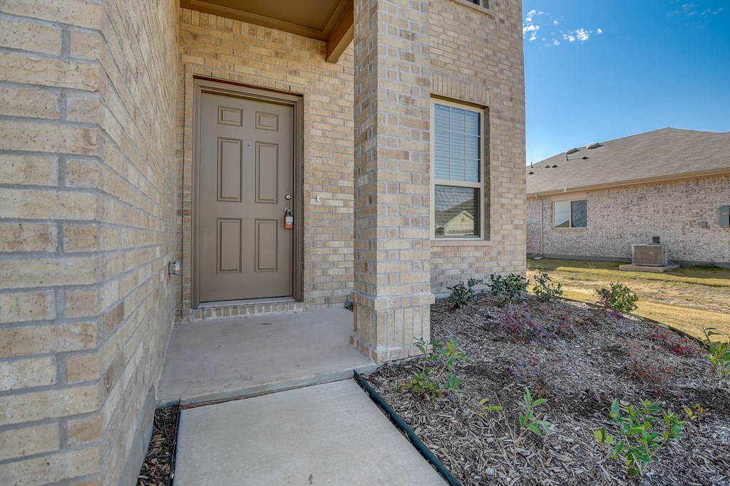 the front door of a brick house with a sidewalk and landscaping