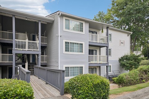 A grey apartment building with a balcony and a small garden.
