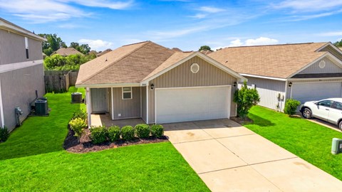 A house with a brown roof and a garage door is surrounded by a well-maintained lawn.