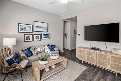 Apartments for Rent in Phoenix AZ - The Crofton at Sheely Farms - Spacious Living Room with a Grey Sofa, Wooden Coffee Table, Armchair, TV Monitor, Mounted TV, and a Ceiling Fan