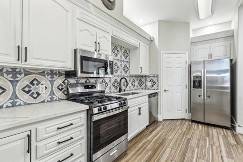 A kitchen with white cabinets and a black and white tiled backsplash.
