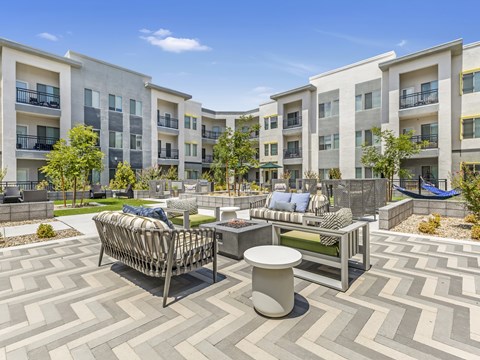 A sunny day at a courtyard with a white and grey patterned floor, a white table and a white sofa.