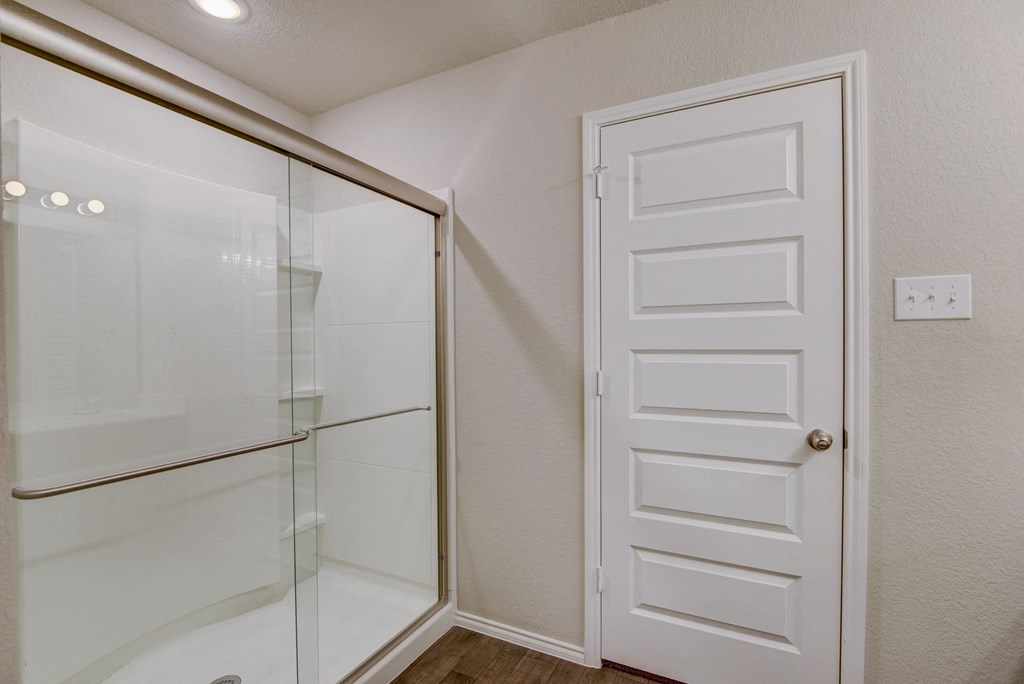 a bedroom with a glass shower and a door to a closet