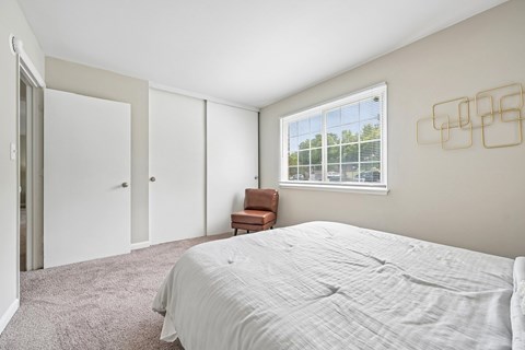 A bedroom with a large bed and a chair by the window.