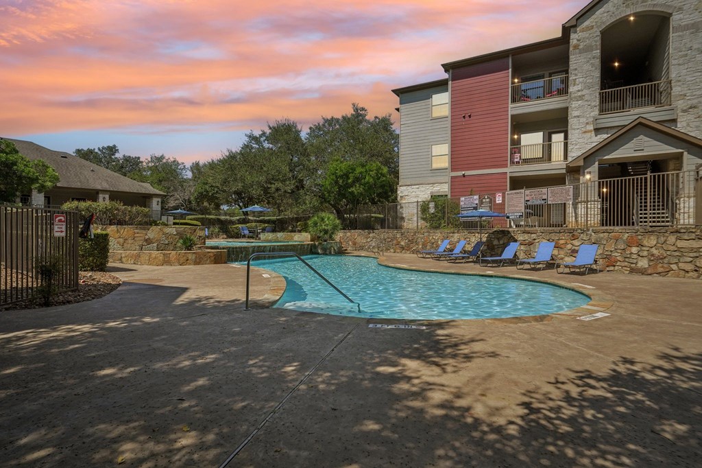 A swimming pool surrounded by a stone wall and chairs.