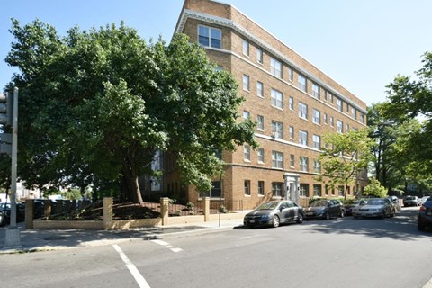 A street view of a row of parked cars in front of a brick building.