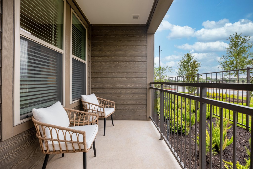 a balcony with two wicker chairs and a view of a yard and the sky