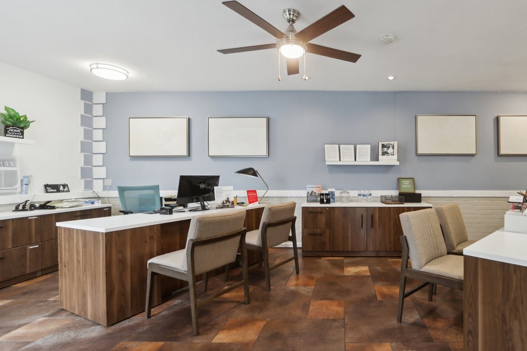A room with a desk, chairs, and a ceiling fan.