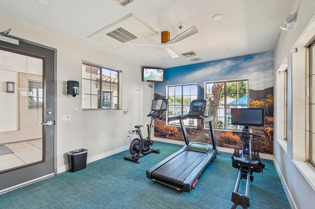 A room with a treadmill, exercise bike, and a television.