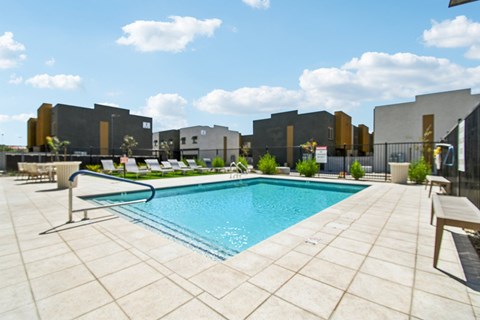 A pool surrounded by a tiled patio and lounge chairs.