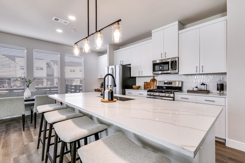 A kitchen with white cabinets and a long island with bar stools.