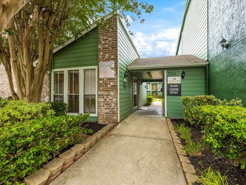 the entrance to a green building with a sidewalk and a tree