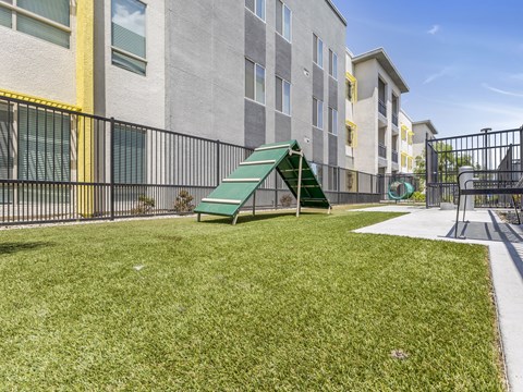 A playground with a green slide and a green bench in front of a grey building.