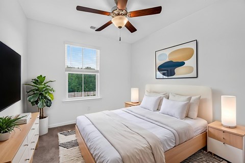 A bedroom with a large bed, a ceiling fan, and a painting on the wall.
