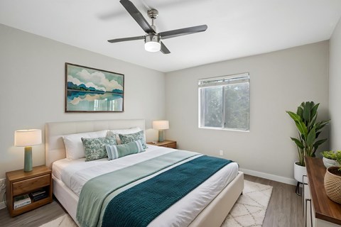 A bedroom with a bed, a ceiling fan, and a painting on the wall.