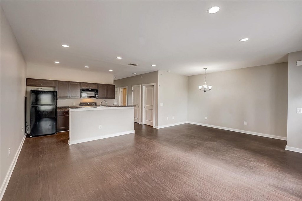 an empty living room with a kitchen in the background