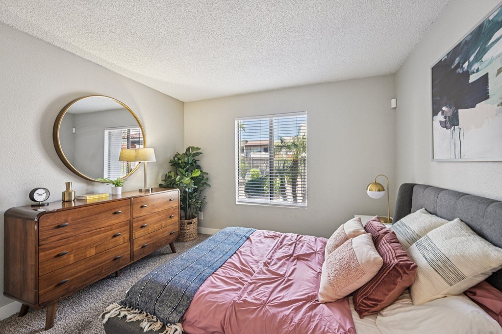 A bedroom with a bed, dresser, mirror, and window.