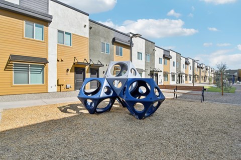 A playground with a blue structure in front of apartment buildings.