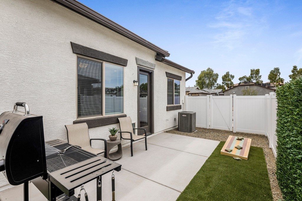 A patio with a grill and chairs is in front of a house.