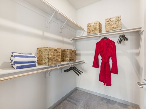 A red robe is hanging on a rack in a white closet.