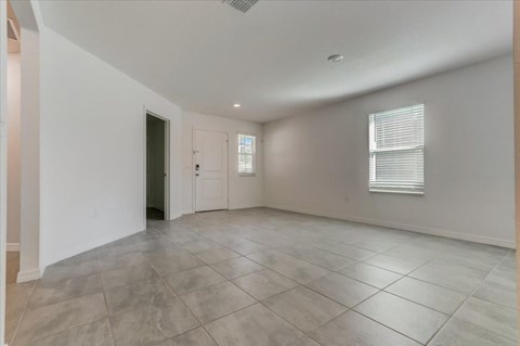 Empty living room with gray tile flooring, white walls, front door, and window.