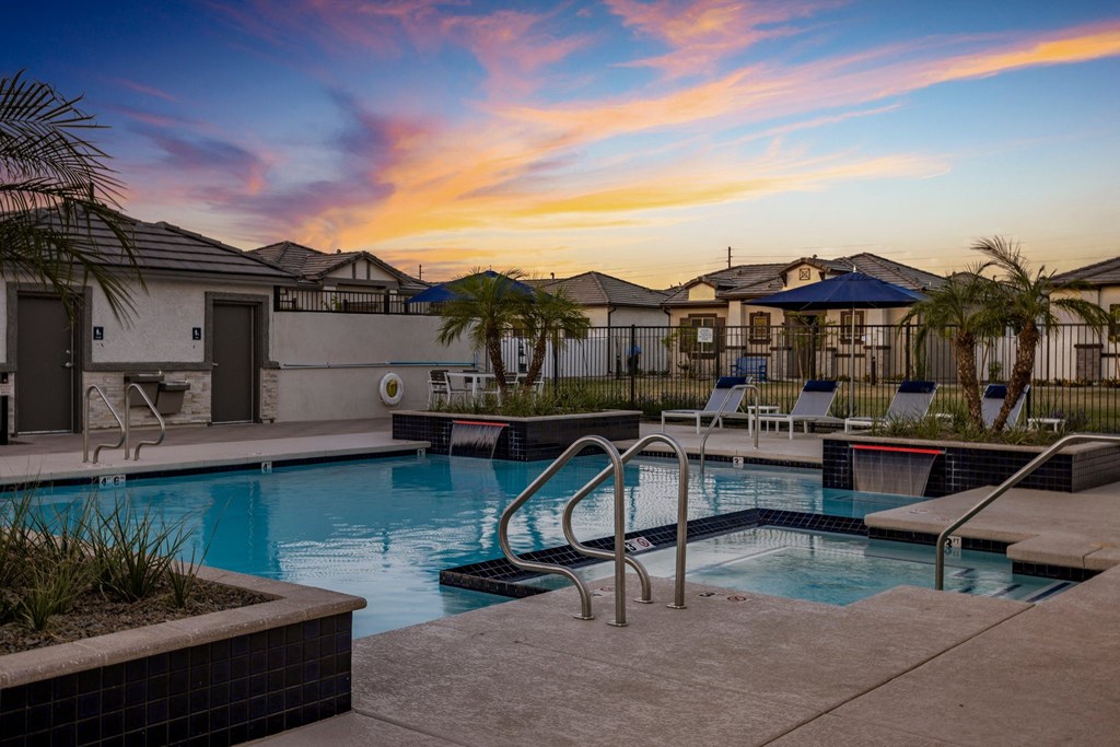 Phoenix AZ Apartments - The Crofton at Sheely Farms - Large Pool with a Hot Tub, Fountains, Plant Beds, Poolside Lounge Chairs, and Umbrellas, Shot at Sunset