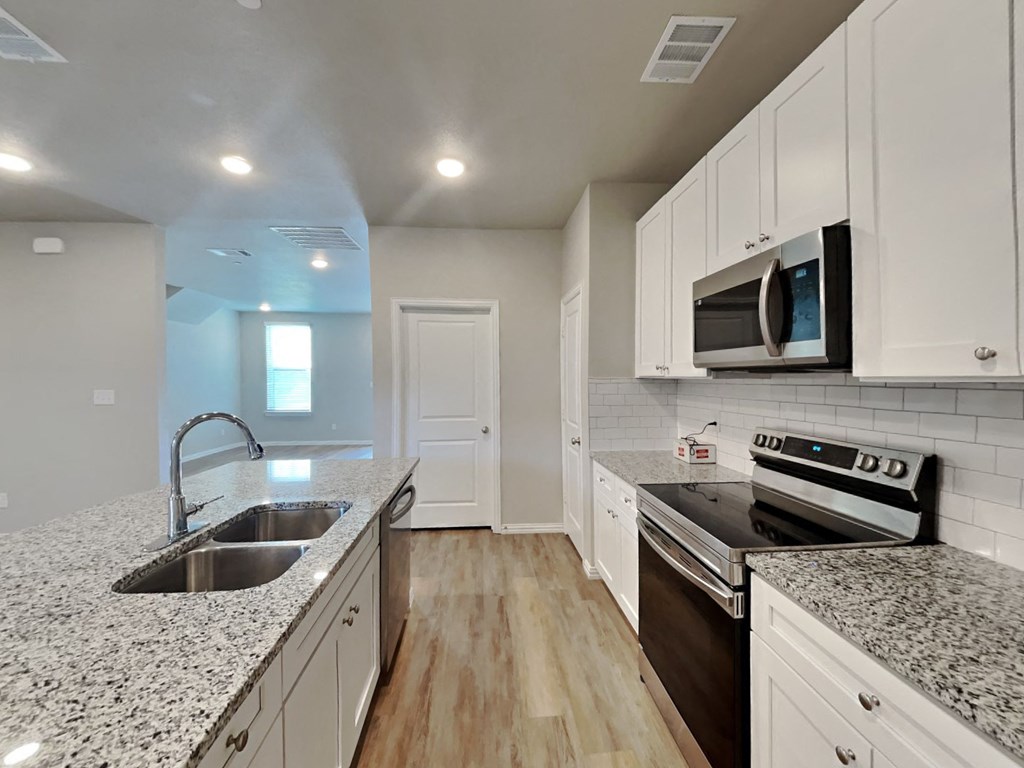 Townhouses In Willow Park, TX For Rent - Willow Crossing Townhomes - Open Concept Kitchen With Granite Countertops, White Cabinets, Kitchen Island, And Stainless Steel Appliances