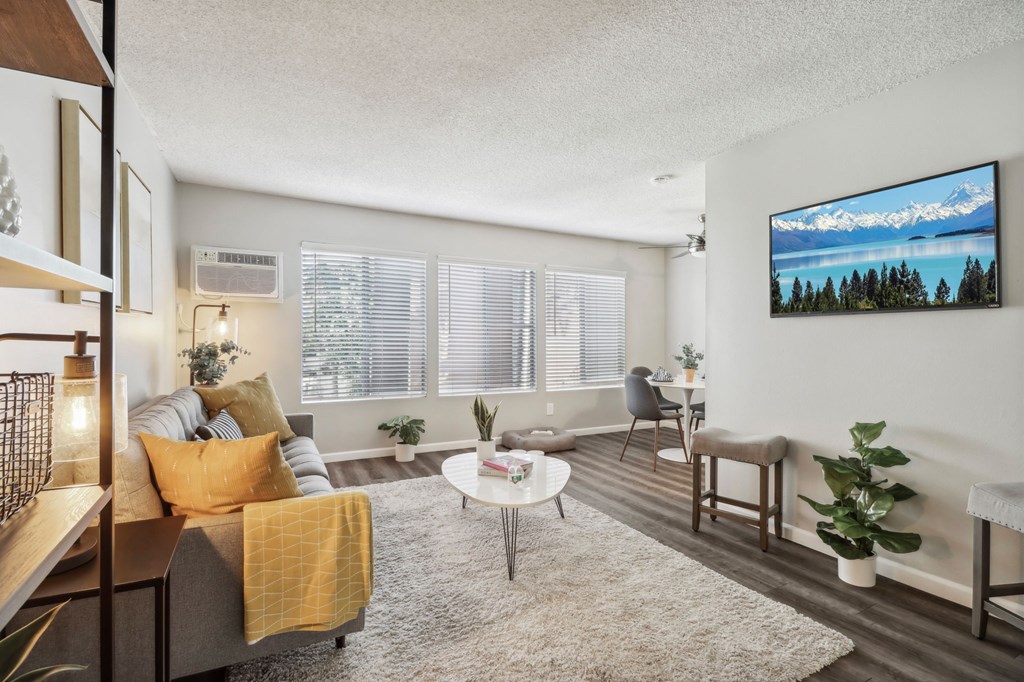 A living room with a grey couch, a yellow throw blanket, a white coffee table, and a flat screen TV mounted on the wall.