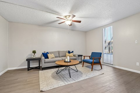 A living room with a grey couch, a blue chair, and a ceiling fan.