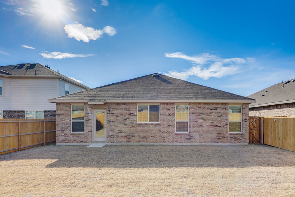 the back of a brick house with a yard and a wooden fence