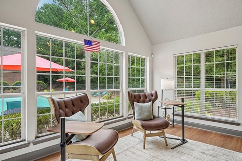 A room with a chair and a table in front of a window with a view of a pool and trees.