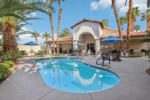 A pool surrounded by palm trees and a building in the background.