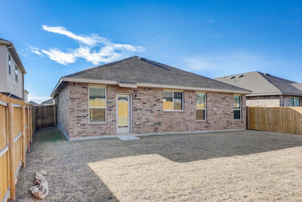 the back of a brick house with a yard and a fence
