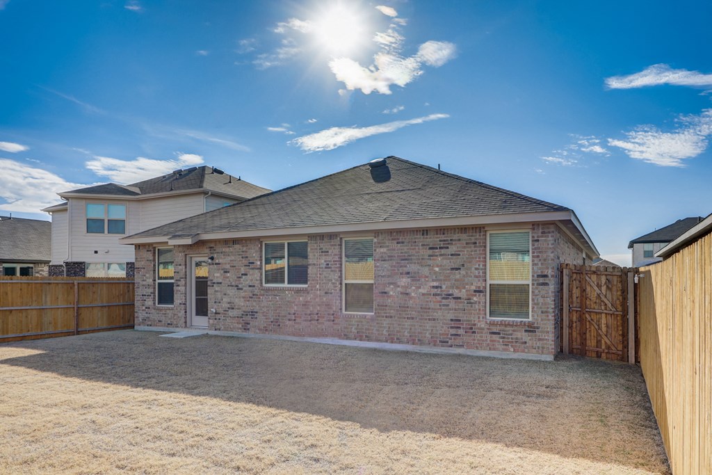 the back of a brick house with a driveway and a wooden fence