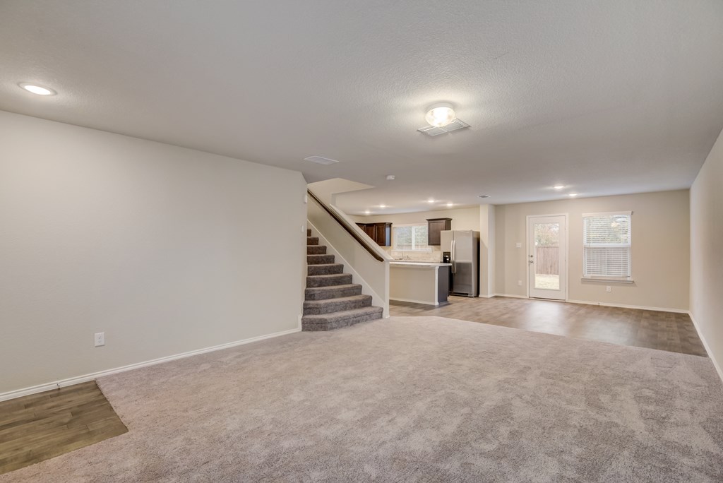 an empty living room with a staircase and a kitchen
