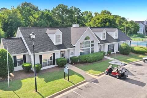 A white house with a grey roof and a red golf cart parked in front.